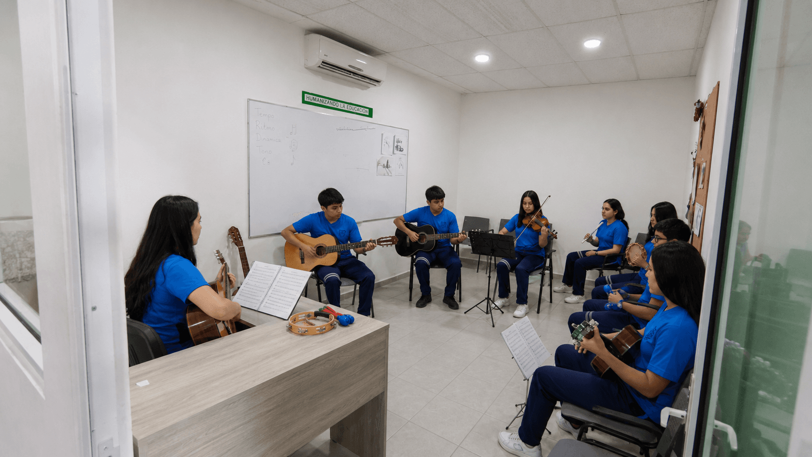 Estudiantes ensayan guitarra, violín y percusiones en el salón de música